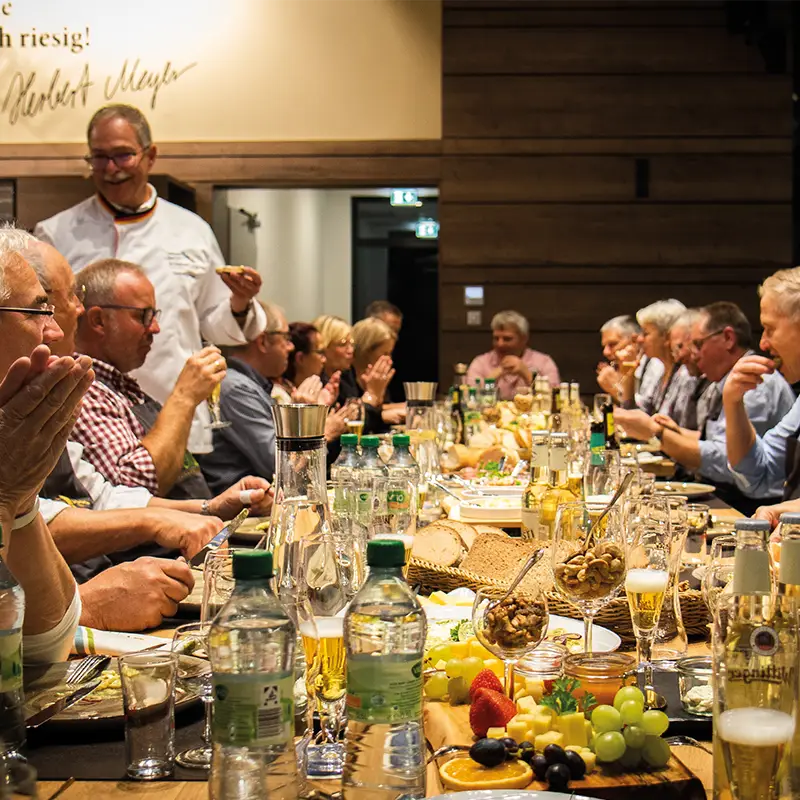 AbendBrot Mehrere Personen sitzen am reichlich gedeckten Tisch beim AbendBrot Event, essen gemeinsam und hören Herbert Meyer zu